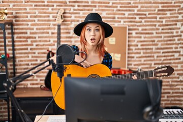 Fototapeta na wymiar Young caucasian woman playing classic guitar at music studio scared and amazed with open mouth for surprise, disbelief face