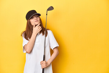 Redhead golfer with club and cap, studio shot looking sideways with doubtful and skeptical expression.
