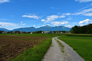 Fototapeta na wymiar Road leading to a village at Sorsko polje and mountain Storzic behind in Gorenjska, Slovenia