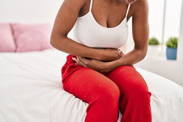 African american woman suffering for menstrual pain sitting on bed at bedroom