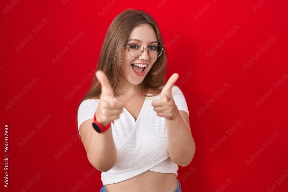 Sticker Young caucasian woman standing over red background pointing fingers to camera with happy and funny face. good energy and vibes.