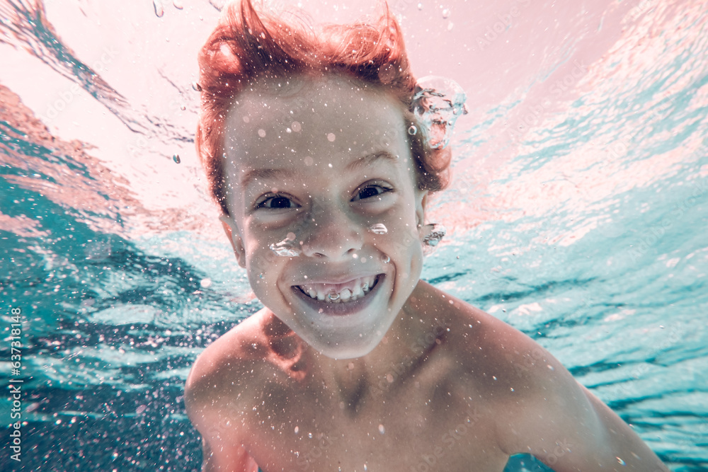 Wall mural Cheerful boy swimming underwater in pool