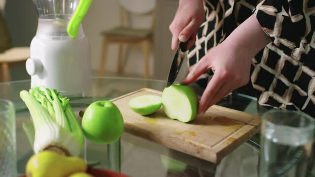 Close up of female hands cutting apples on wooden cutting board to make smoothie in electric mixer