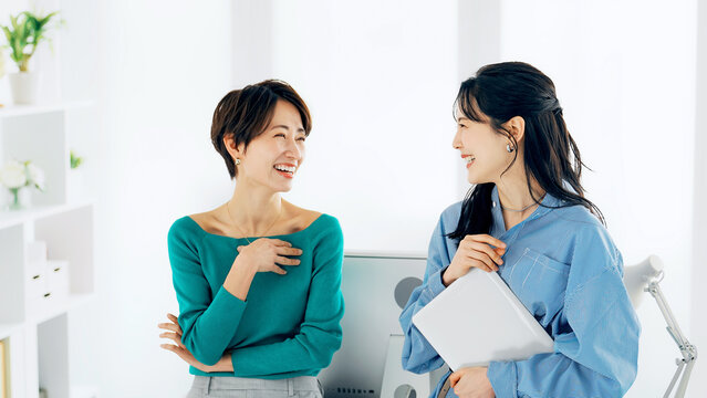 オフィスでノートパソコンを見ながら話す二人の女性