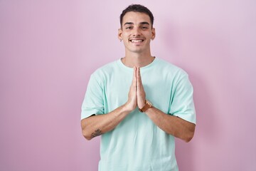 Handsome hispanic man standing over pink background praying with hands together asking for...