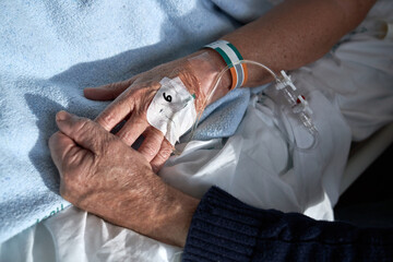 Crop anonymous elderly male holding hand of sick wife in clinic