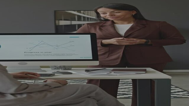 Vertical medium shot of young Biracial female office worker talking to colleague at workplace