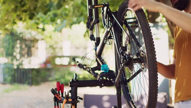 Sports-loving man engrossed in fixing modern bicycle with professional equipment. Active caucasian male cyclist confidently repairing bike chain and examining tire for summer leisure cycling.