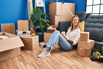 Young hispanic woman drinking coffee sitting on floor at new home