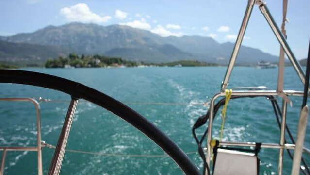 View from the stern to the trail of a boat on the blue water of the Adriatic Sea. The steering wheel of a sailing yacht. Sunny day in the Kotor Bay of Montenegro.