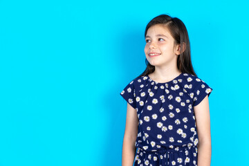 Caucasian kid girl wearing floral dress over blue background  looking aside into empty space thoughtful