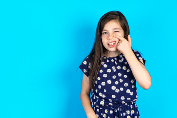 Caucasian kid girl wearing floral dress over blue background  pointing unhappy to pimple on...