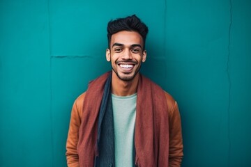 Portrait of a happy young indian man standing against blue wall