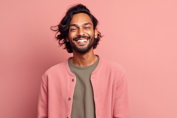 Fototapeta premium Cheerful indian young man smiling and looking at camera while standing against pink background