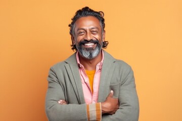 Obraz premium Portrait of a happy indian man standing with arms crossed against orange background