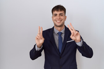 Young hispanic business man wearing suit and tie smiling looking to the camera showing fingers doing victory sign. number two.