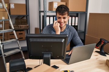 Young hispanic man ecommerce business worker using laptop talking on smartphone at office