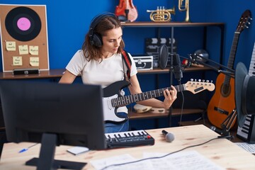 Young woman artist singing song playing electrical guitar at music studio