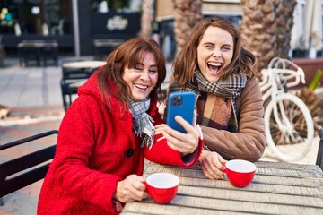 Two women mother and daughter using smartphone drinking coffee at coffee shop terrace