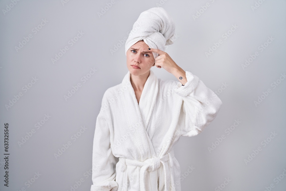 Poster Blonde caucasian woman wearing bathrobe pointing unhappy to pimple on forehead, ugly infection of blackhead. acne and skin problem