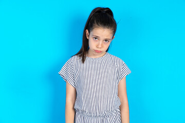 Caucasian kid girl wearing striped dress over blue background depressed and worry for distress,...