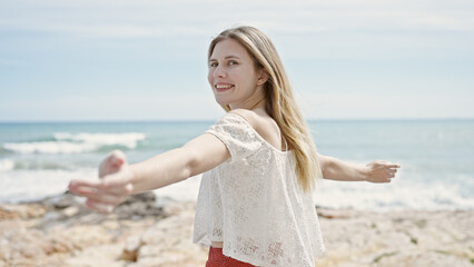 Fototapeta na wymiar Young blonde woman tourist smiling confident standing with arms open at beach
