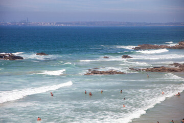 Vibrant scene at Porto Covo's expansive beach: bathers enjoying the waves, basking in the sun, and playing in the sea's embrace.