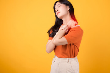 Obraz premium Vigilant Asian woman in her 30s, wearing an orange shirt, holds her painful neck on yellow background. office syndrome health care concept.