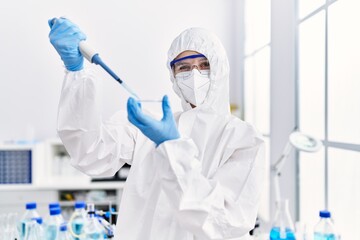 Young blonde woman scientist wearing security uniform pouring liquid on sample at laboratory