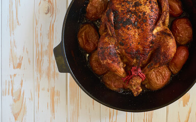 Oven-roasted baked chicken with apples in cast iron skillet pan on the white wooden background food...