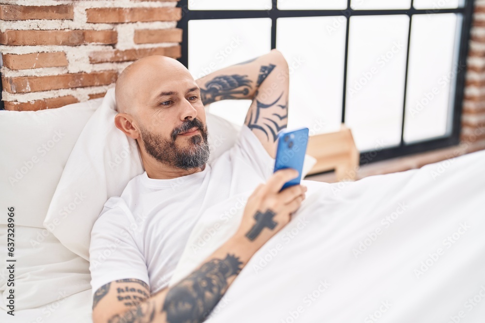 Canvas Prints Young bald man using smartphone lying on bed at bedroom