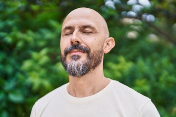 Young bald man breathing with closed eyes at park