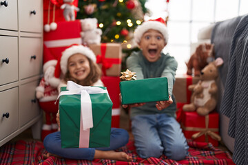 Obraz na płótnie Canvas Two kids holding gift sitting on floor by christmas tree at home