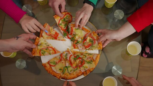 Top view tasty delicious pizza on table with Caucasian male and female hands taking slices in slow motion leaving. Unrecognizable young men and women partying indoors enjoying junk food