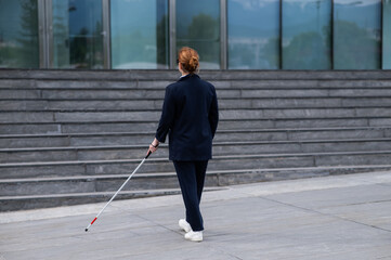 Blind businesswoman walking with tactile cane to business center. 