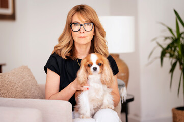 Smiling mid aged woman relaxing in an armchair in her modern home with her cute dog