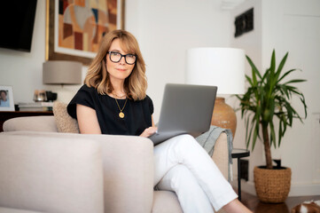 Attractive mid aged woman with notebook sitting in an armchair and working online from home