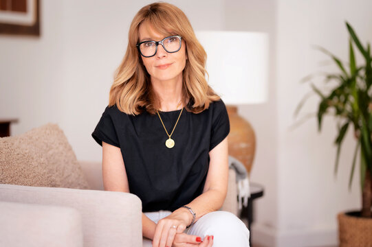 Confident mid aged woman wearing cassual clothes and relaxing in an armchair in her modern home