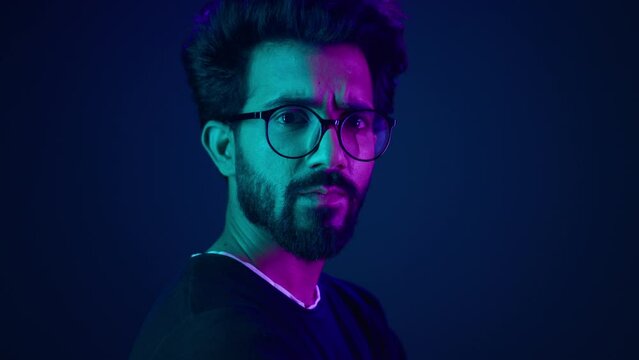 Close up male portrait in neon ultraviolet blue background Indian man Muslim Arabian guy posing in profile turning head looking at camera with serious face expression hacker developer coding worker