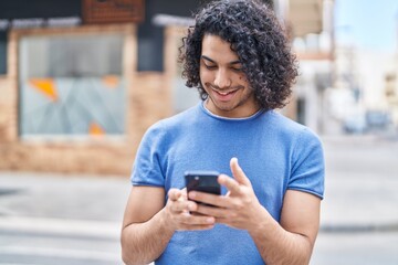 Fototapeta na wymiar Young latin man smiling confident using smartphone at street