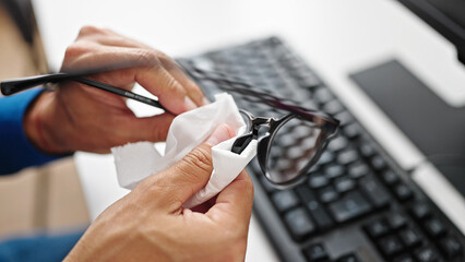 Young hispanic man cleaning glasses at office