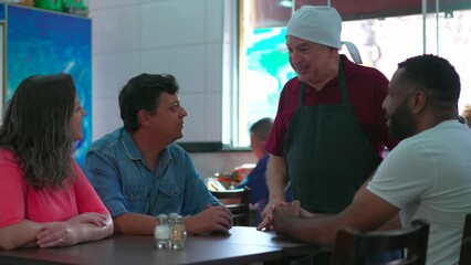 Male waiter taking orders from customers at restaurant. Brazilian scene of employee speaking with a group diverse of people in traditional cafeteria