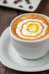 Patterned cappuccino coffee in a white porcelain cup on a wooden table