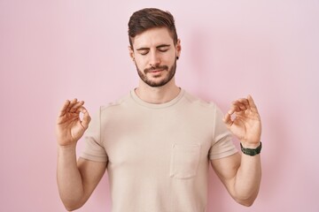 Hispanic man with beard standing over pink background relaxed and smiling with eyes closed doing meditation gesture with fingers. yoga concept.