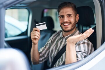 Hispanic man with beard driving car holding credit card celebrating achievement with happy smile...
