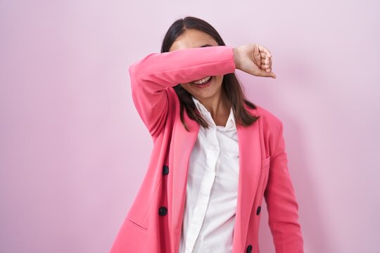 Young hispanic woman wearing business clothes and glasses covering eyes with arm smiling cheerful and funny. blind concept.