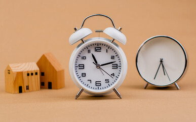 time and home white alarm clock with small model wooden house home loan finance and time