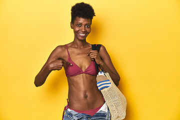 African woman in bikini carrying beach bag, summer concept, person pointing by hand to a shirt copy space, proud and confident