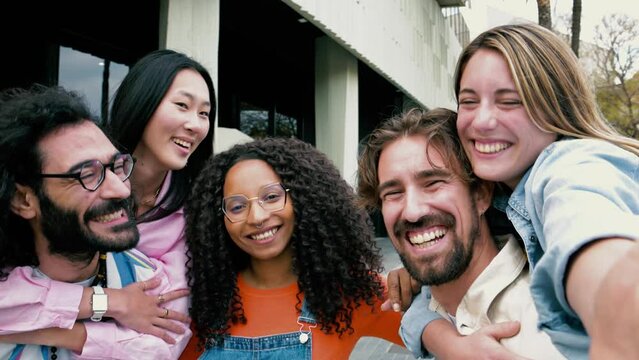 Diverse group of friends laughing hugging each other and taking a selfie in the street.Cheerful multiracial group of young hipsters taking a picture outside and looking at camera.