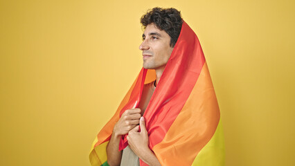 Young hispanic man wearing rainbow flag with relaxed expression over isolated yellow background